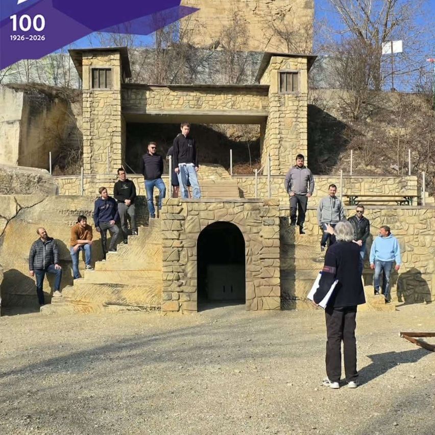 A group of people are gathered in front of a stone structure with a tunnel entrance, likely on a historical site. They are posing for a photograph.