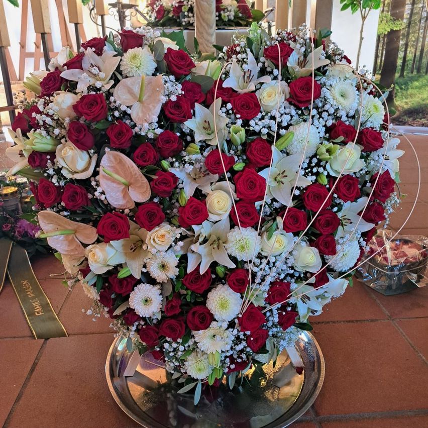 Eine große herzförmige Blumen-Arrangement mit roten, weißen und rosa Rosen, Lilien und Babys atmen auf einer silbernen Platte.