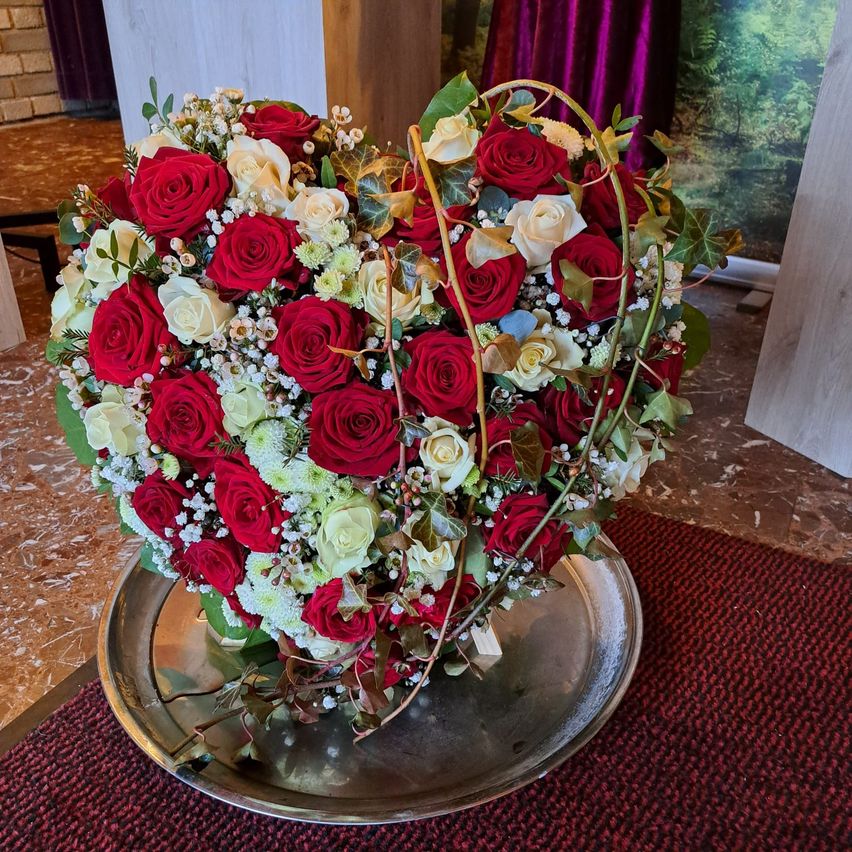 A heart-shaped bouquet of red and white roses with green leaves and baby's breath sits on a silver tray on a red carpet.