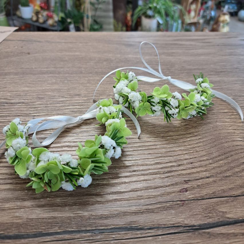 Zwei Blumenkränze mit weißen und grünen Blumen auf einem Holztisch.