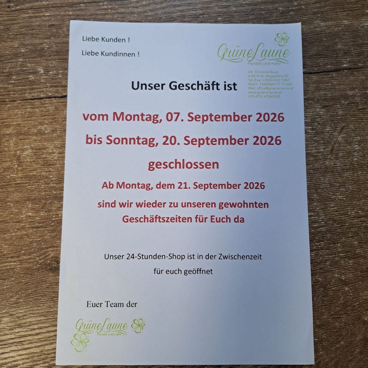 Ein weißer Flyer auf einer Holzoberfläche kündigt an, dass der Laden vom 7. September bis zum 20. September 2026 geschlossen ist. Er öffnet am 21. September 2026 wieder. Der 24-Stunden-Shop des Ladens bleibt in dieser Zeit geöffnet.