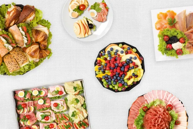 Eine Vielzahl von Sandwiches, Obst und Fleisch ist auf einer weißen Oberfläche ausgestellt. Es gibt sechs Teller und eine Platte.