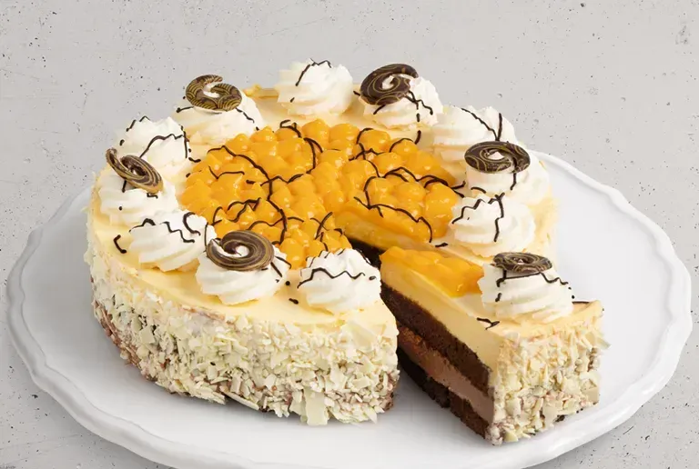 Eine Scheibe Kuchen mit Schokoladen- und Mangoschichten liegt auf einem weißen Teller. Es ist mit Schlagsahne und Wirbeln garniert.