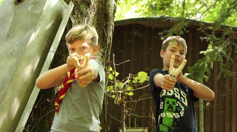 Zwei Jungen stehen in einem Waldgebiet. Ein Junge hat einen schädelförmigen Stock in der Hand.