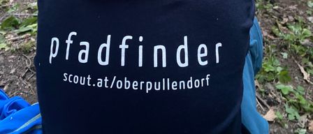 Eine Gruppe von Kindern in Pfadfinderuniformen ist draußen, wobei ein Kind ein blaues Hemd mit dem Wort Pfadfinder trägt.