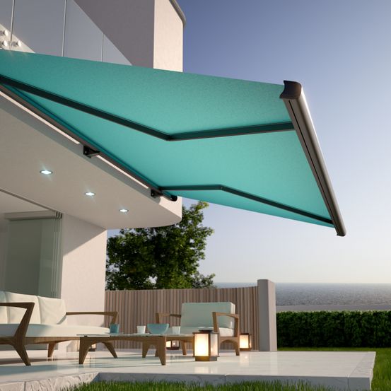 Eine Außenterrasse mit einem modernen Haus, ausgestattet mit einem versenkbaren Vordach über einer Terrassengarnitur mit Tischen, Tassen und Lampen. Die Terrasse ist von einem Holzzaun umgeben mit Blick auf das Meer.