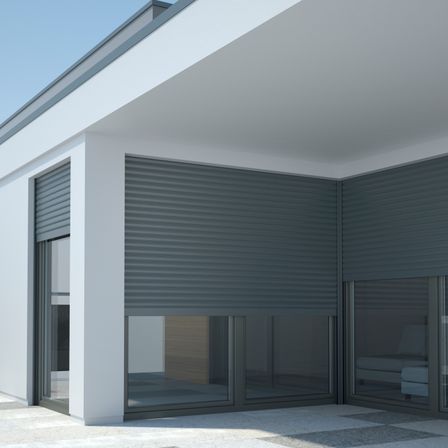 Modernes Hausaußen mit grauen Rollladen-Jalousien und Glastüren, die den klaren blauen Himmel widerspiegeln.