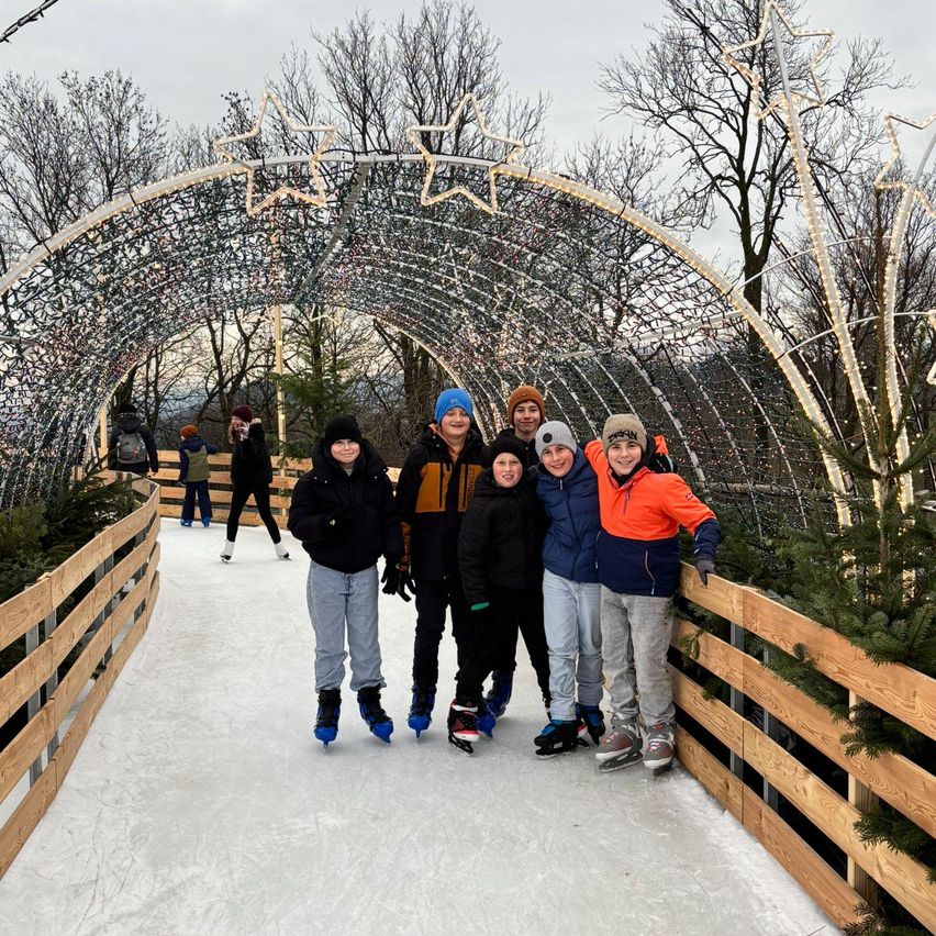 Eine Gruppe von Menschen in Winterkleidung und Schlittschuhen posiert für ein Foto auf einer Eisbahn mit einem dekorativen Torbogen.
