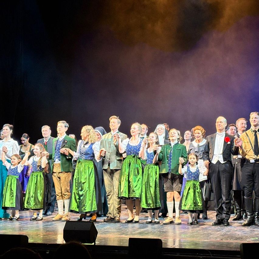 Eine Bühne voller Darsteller in traditioneller Kleidung, wahrscheinlich nach einer Aufführung, mit Nebel und Scheinwerfern im Hintergrund.