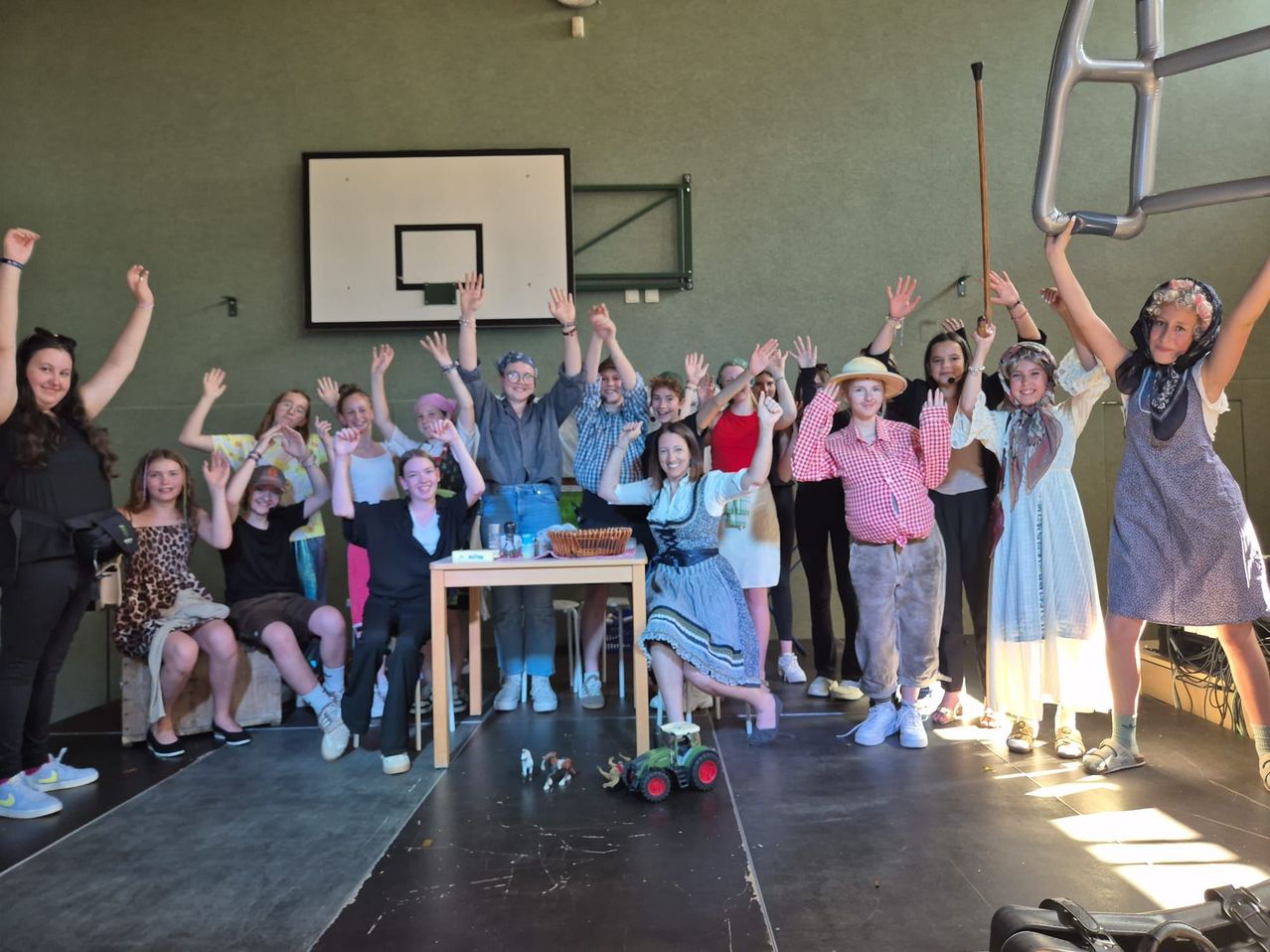 Eine Gruppe von Menschen in verschiedenen Kostümen, einige sitzend und andere stehend, posiert für ein Foto in einem Raum mit einem Basketballkorb.