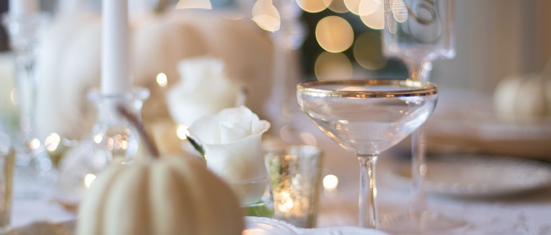 Ein Tisch ist für einen festlichen Anlass gedeckt mit einer weißen Kürbis, weißen Rosen und Weinglas. Eine Kerze leuchtet sanft.
