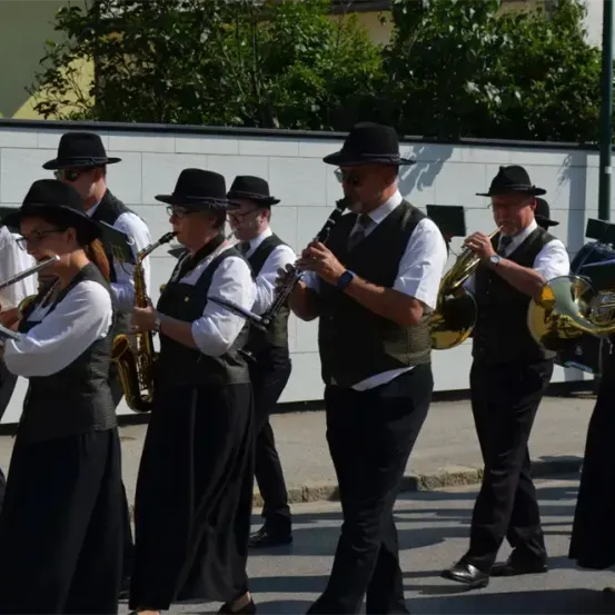 Eine Gruppe von Musikern in schwarzen Hüten und Uniformen spielt verschiedene Instrumente im Freien.