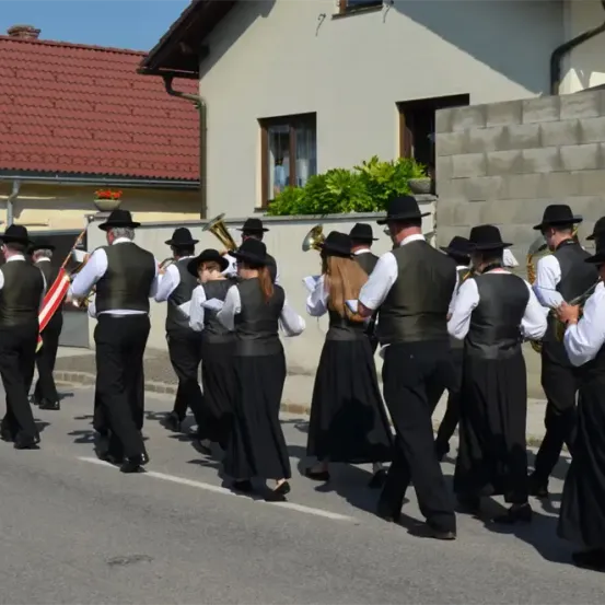 Eine Blaskapelle tritt auf der Straße auf. Einige Mitglieder spielen Blechblasinstrumente, während andere singen.
