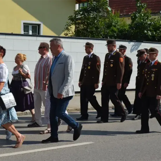 Eine Gruppe von Menschen in Uniform und andere in Freizeitkleidung gehen in einem Umzug die Straße entlang.