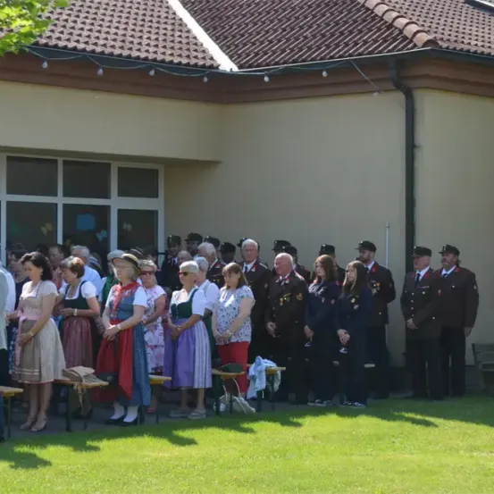 Eine vielfältige Gruppe von Menschen steht vor einem Gebäude, einige in Uniformen und andere in Freizeitkleidung, mit einer Bank und Topfpflanzen im Vordergrund.