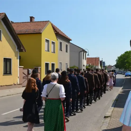 Eine Gruppe von Menschen in Uniformen marschiert eine Straße mit gelben Häusern und einem klaren Himmel hinunter.