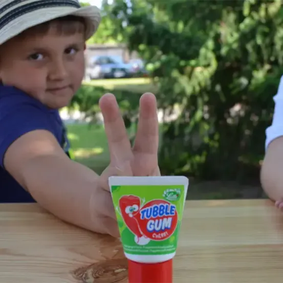 Ein junger Junge sitzt an einem Tisch, hält eine Tube Tic Tac Kaugummi in der Hand und macht ein Friedenszeichen.