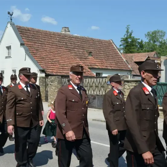 Eine Gruppe uniformierter Personen, wahrscheinlich Militärangehörige, geht vor einem Gebäude mit Giebeldach die Straße entlang.