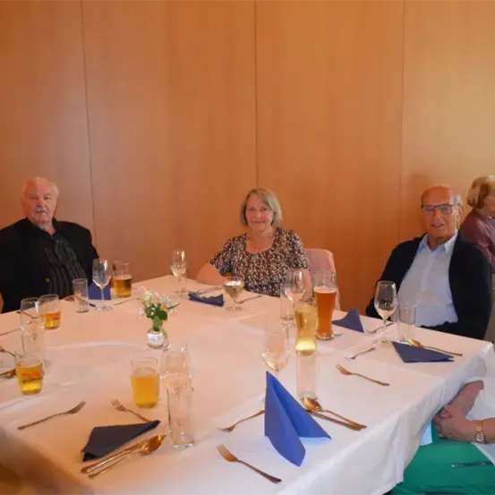 Eine Gruppe älterer Menschen versammelt sich um einen Tisch in einem Restaurant und genießt Getränke und Essen.