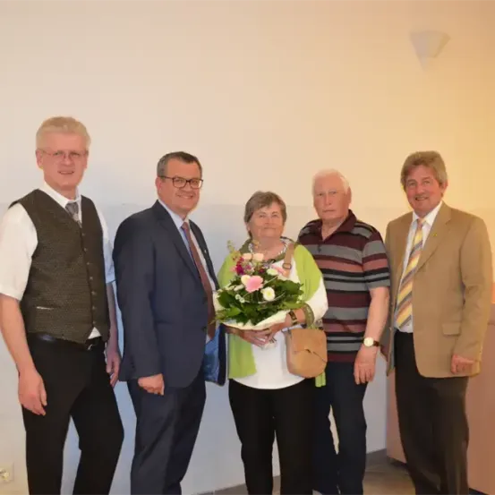 Fünf Personen posieren für ein Foto in einem Büroraum. Die Frau hält einen Blumenstrauß.