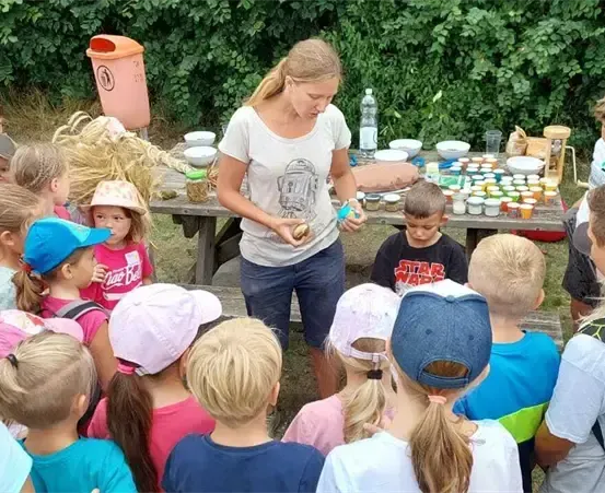 Eine Frau unterrichtet eine Gruppe von Kindern im Freien um einen Tisch mit Gläsern mit Lebensmitteln und einem Mülleimer.