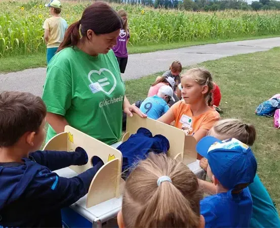 Eine Frau in einem grünen T-Shirt leitet eine Gruppe von Kindern, die Kleidung in einem Feld sortieren.
