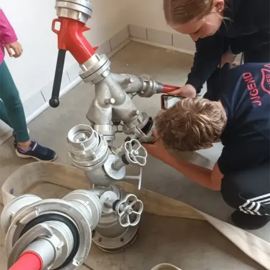 Zwei Personen arbeiten an einem großen Metallrohrventil, einer kniet und der andere steht dahinter, beide scheinen sich auf die Aufgabe zu konzentrieren.