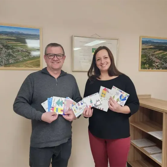 Ein Mann und eine Frau halten Weihnachtskarten in einem Raum mit einem Bücherregal und gerahmten Bildern an der Wand.