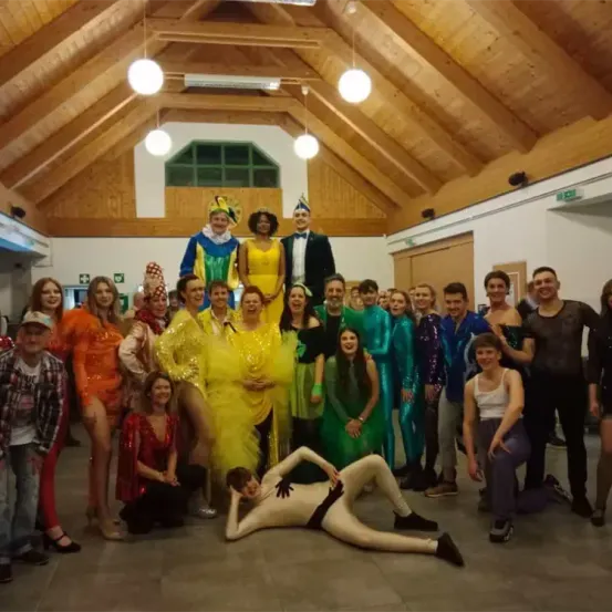 Eine Gruppe von Menschen in Kostümen posiert für ein Foto in einem Raum mit Holzbalken und Lichtern.