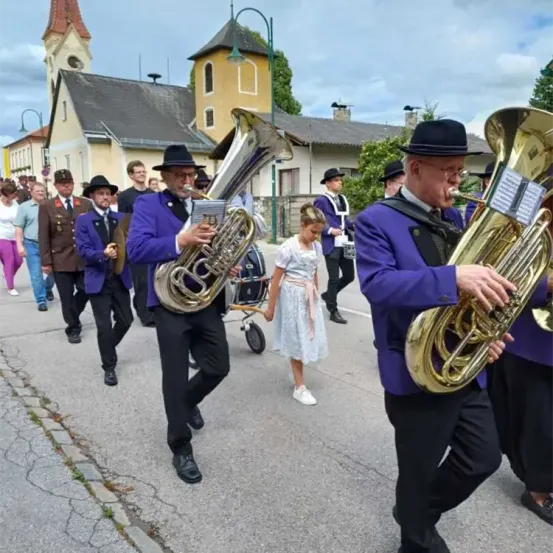 Eine Blaskapelle spielt auf Tubas und geht auf einer Straße vor einem Gebäude.