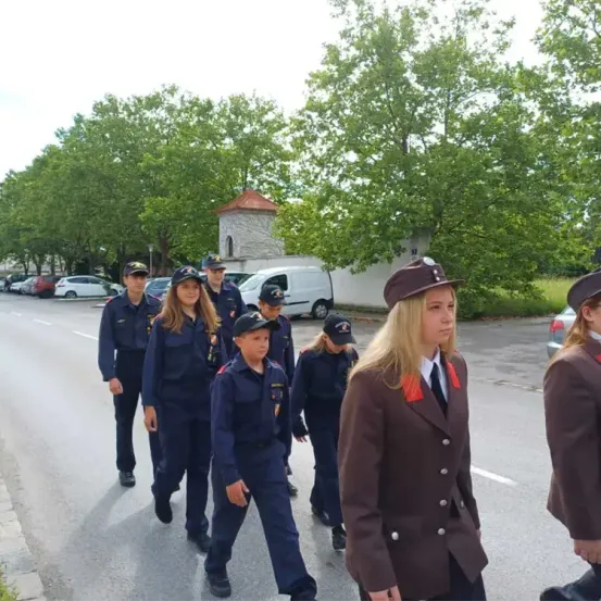 Eine Gruppe uniformierter junger Menschen geht eine Straße entlang. Bäume säumen die Straße auf beiden Seiten. Im Hintergrund ist ein weißer Van geparkt.