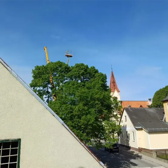 Ein Luftbild einer kleinen Stadt mit einer Kirche, einem Kran und einem Haus. Die Kirche hat einen Turm und ein rotes Dach. Ein Auto ist am Straßenrand geparkt.