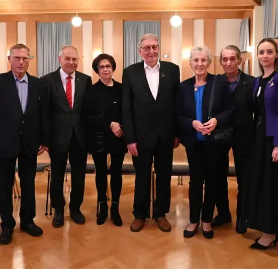 Eine Gruppe formell gekleideter Personen, einschließlich Männer und Frauen, steht gemeinsam in einem Raum. Sie lächeln und scheinen für ein Foto zu posieren.