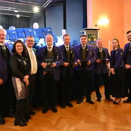 Eine Gruppe von Menschen, Männern und Frauen, gekleidet in formeller Kleidung, steht zusammen in einem Raum mit Musikinstrumenten im Hintergrund. Sie scheinen bei einer Preisverleihung zu sein.