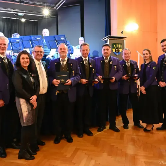Eine Gruppe von Menschen, Männern und Frauen, gekleidet in formeller Kleidung, steht zusammen in einem Raum mit Musikinstrumenten im Hintergrund. Sie scheinen bei einer Preisverleihung zu sein.