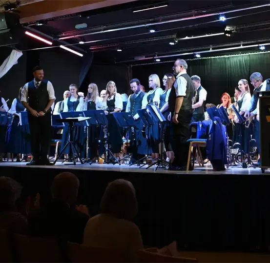 Ein musikalischer Auftritt auf einer Bühne mit Musikern, darunter ein Mann in einem schwarzen Vest, der vorne steht.