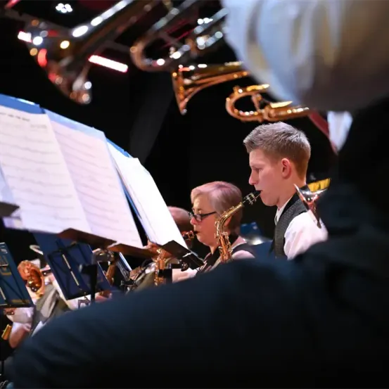 Eine Gruppe von Musikern spielt verschiedene Instrumente während eines Konzerts, wobei ein Saxophonist im Vordergrund und ein Trompeter dahinter zu sehen ist.