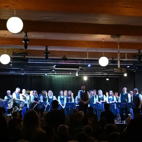 Eine Band spielt auf einer Bühne mit Musikinstrumenten, während ein Publikum zuschaut. Die Bühne ist gut beleuchtet, und die Bandmitglieder stehen vor ihren Instrumenten.