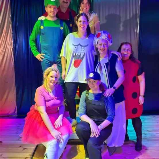 Eine Gruppe von Menschen in Kostümen posiert für ein Foto auf der Bühne. Eine Person sitzt und andere stehen dahinter.