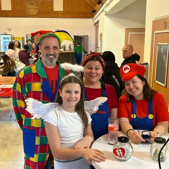 Eine Gruppe von Erwachsenen und Kindern in Kostümen, möglicherweise für eine Party, mit einer Uhr an der Wand und anderen im Hintergrund.