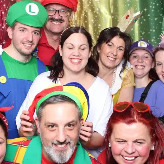 Eine Gruppe von Menschen in Kostümen und Hüten posiert für ein Foto vor einem farbenfrohen Hintergrund.