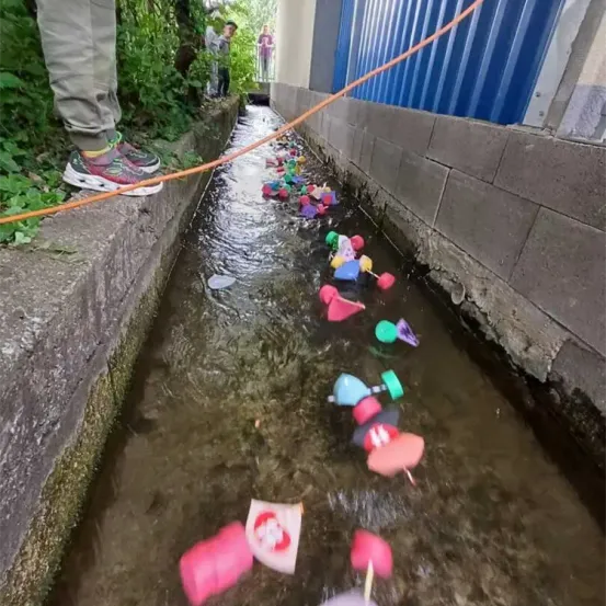 Ein Blick auf einen schmalen Bach mit verschiedenen bunten Plastikspielzeug im Wasser. Eine Person steht in der Nähe des Baches.
