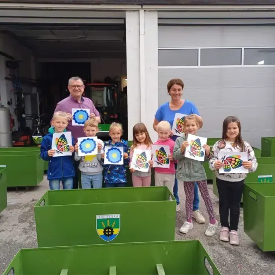 Eine Gruppe von Kindern, zusammen mit zwei Erwachsenen, posiert für ein Foto, während sie Schmetterlingszeichnungen vor einem Gebäude halten.
