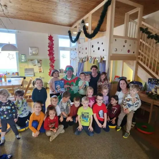 Eine Gruppe von Kindern und Erwachsenen versammelt sich in einem Raum mit einem Weihnachtsbaum und Dekorationen. Sie lächeln und posieren für ein Foto.