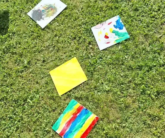 Fünf farbenfrohe Gemälde sind auf einem grünen Feld verteilt. Eines ist weiß, ein anderes gelb und die anderen sind farbenfroh. Das Gras ist üppig.