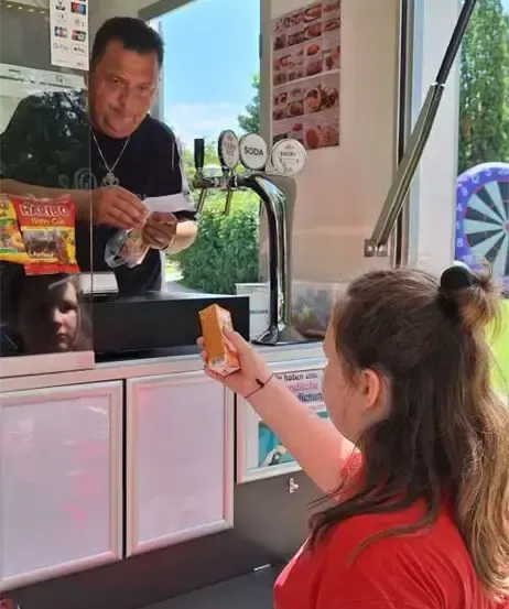 Ein Mann und eine Frau sind in einem Foodtruck. Der Mann bereitet eine Bestellung vor, während die Frau eine Packung Snacks in der Hand hält.