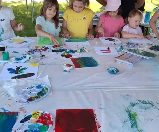 Eine Gruppe junger Kinder sitzt um einen Tisch herum und ist mit einer Kunstaktivität beschäftigt. Sie malen mit verschiedenen Farben auf Papier.