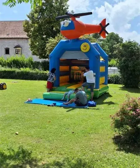 Eine Gruppe von Menschen spielt an einem sonnigen Tag in einem blauen und orangefarbenen Hubschrauber-Bouncy-House.