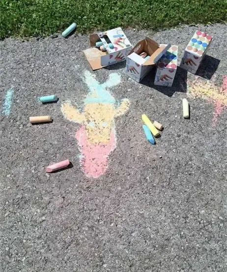 Ein Außenbereich mit einer Zeichnung eines Charakters, die mit Kreide gemacht wurde. Einige Buntstifte und Kisten sind herum verstreut.