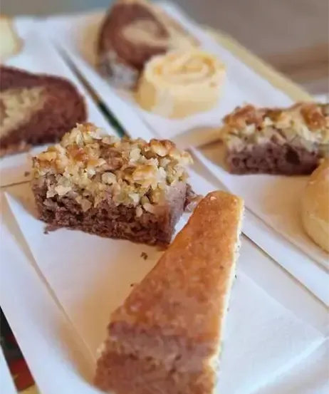 Auf dem Tisch sind verschiedene Desserts, darunter ein Schokoladenkuchen, ein Stück Kuchen und eine Gebäck mit Nüssen. Der Tisch ist mit weißen Tellern gedeckt.